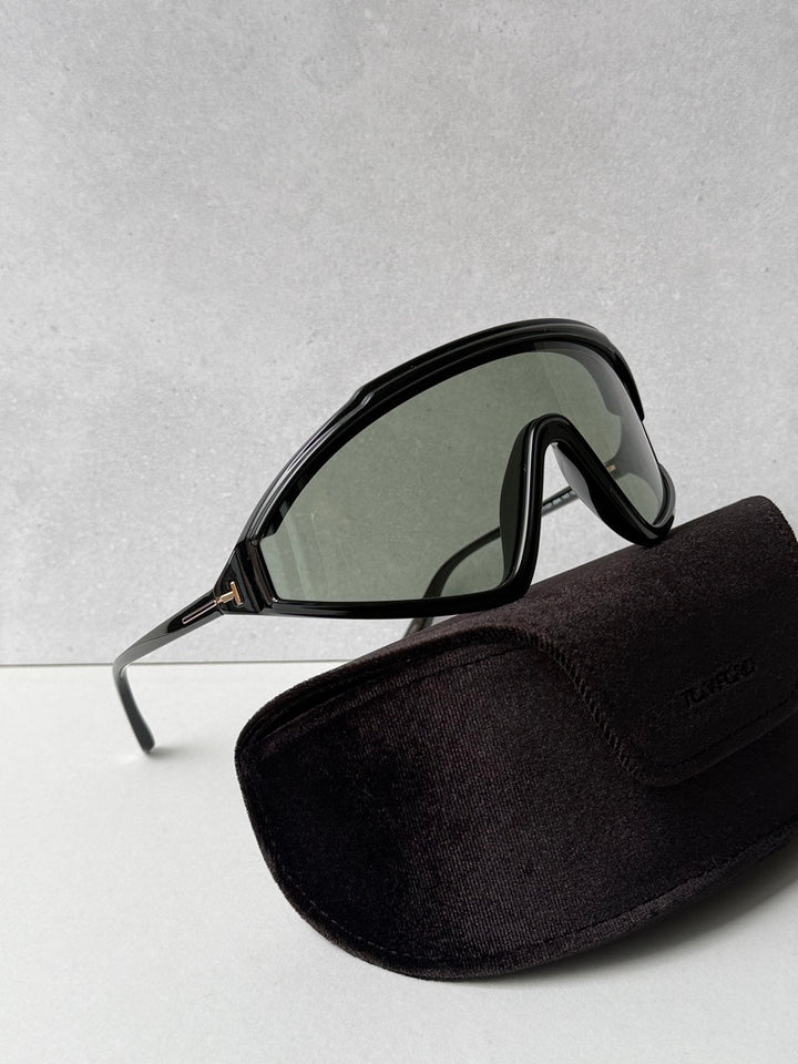 Black sunglasses with dark lenses and curved shield frame, beside black soft case
