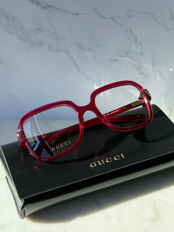 Pink red oversized square eyeglasses on a black Gucci box, clear lenses