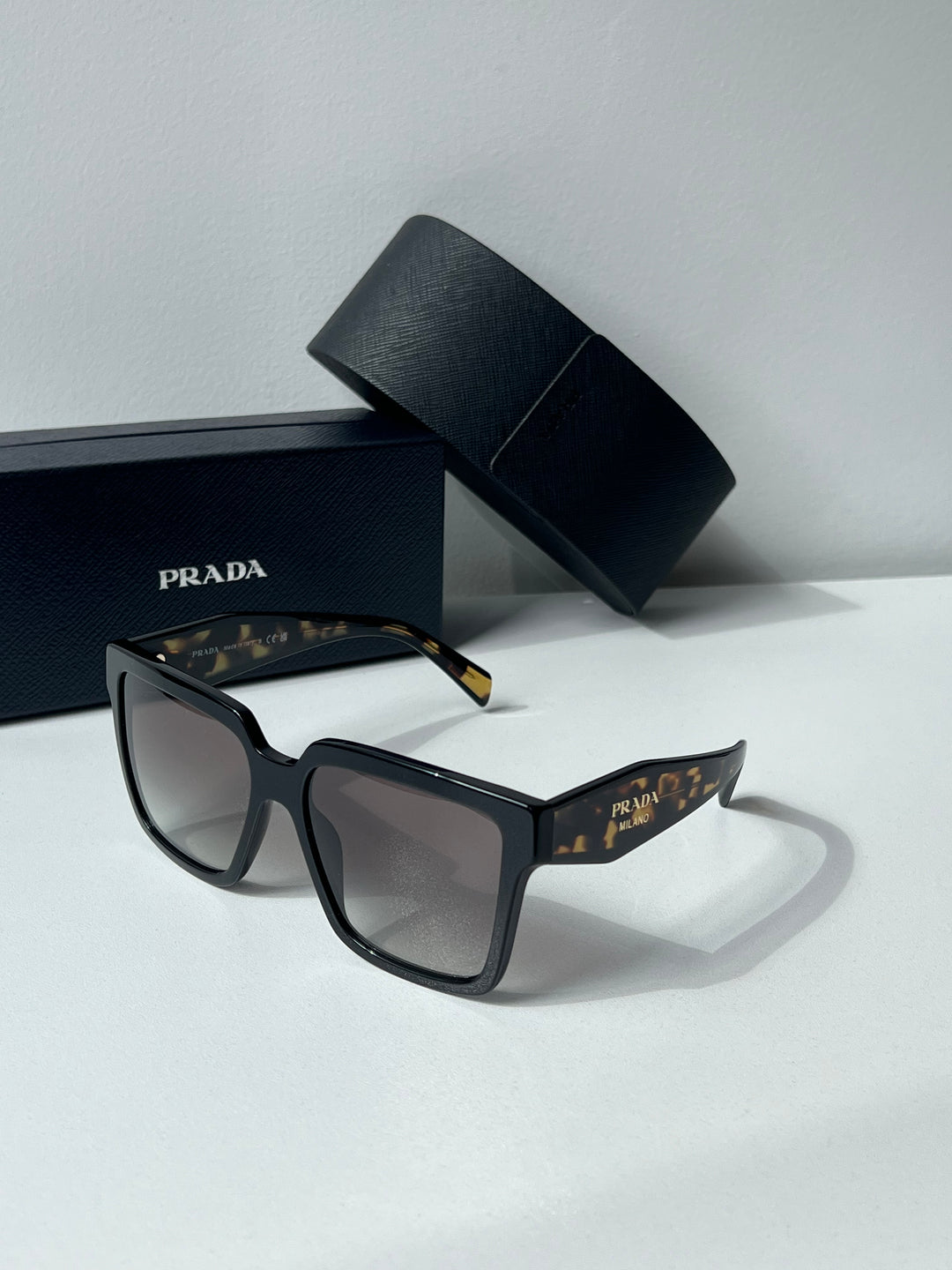 Prada oversized sunglasses with dark lenses, resting with Prada box and case