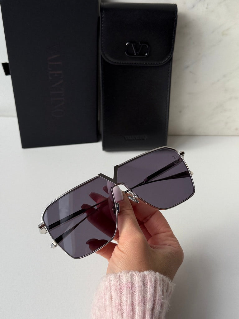 Aviator sunglasses with purple-tinted lenses, held above a black leather case