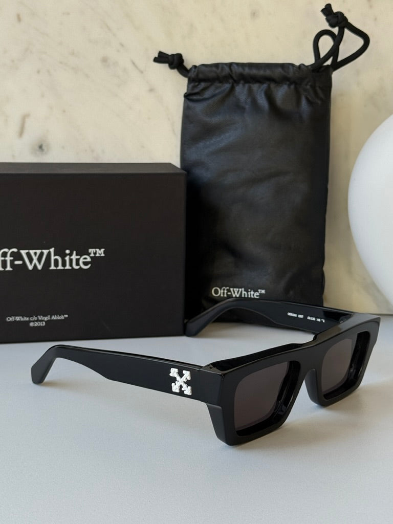 Black sunglasses with dark lenses and Off-White logo, laid out with pouch and box
