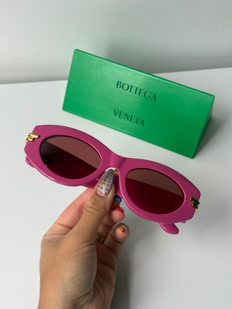 Pink sunglasses held in hand with dark lenses and gold side accents