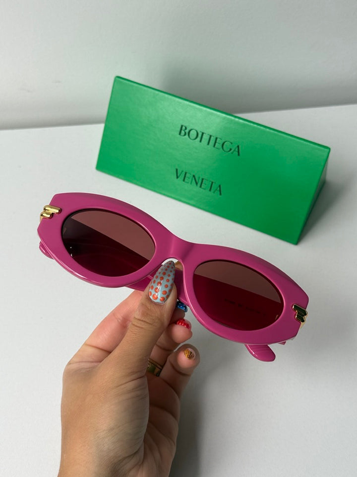 Pink sunglasses held in hand with dark lenses and gold side accents