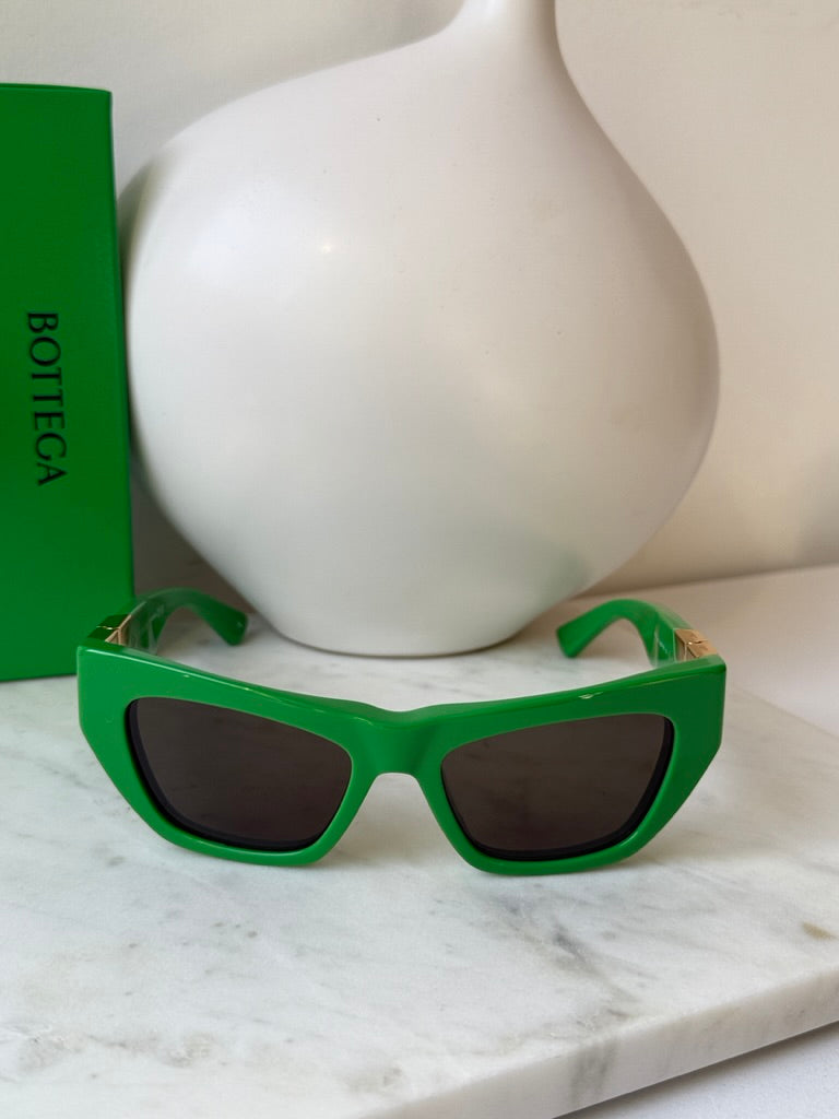 Green cat-eye sunglasses with dark lenses on white display bust