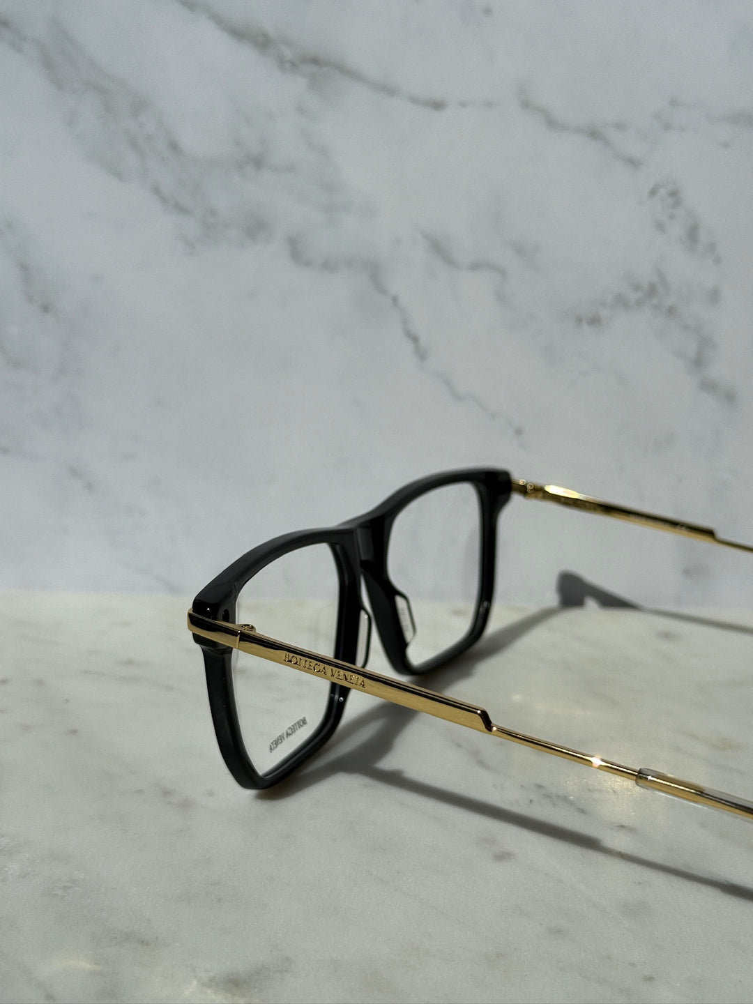 Black eyeglass frame with gold-tone arms and rectangular front, side profile.