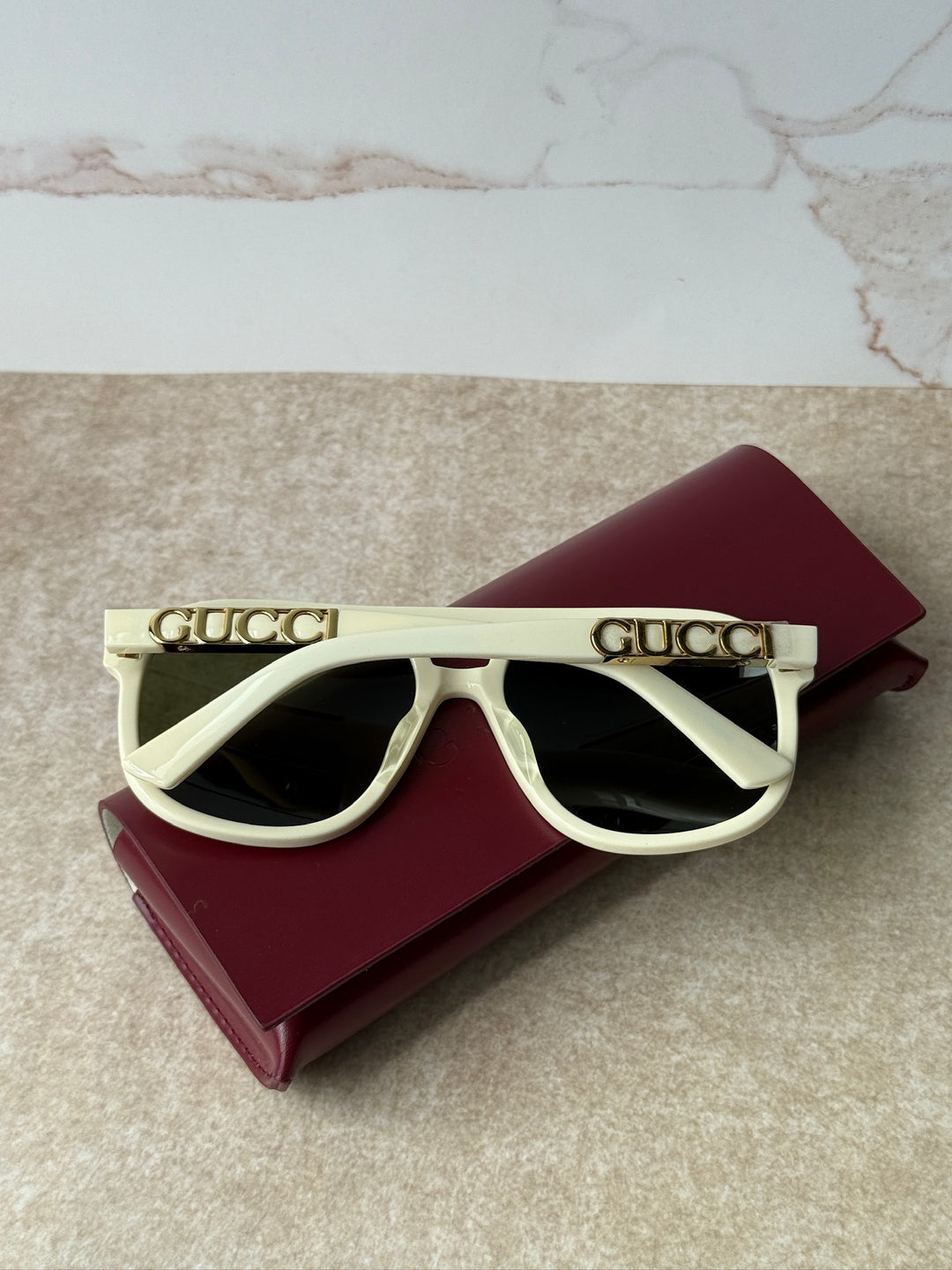 GUCCI aviator sunglasses with ivory frames and dark lenses, front view on burgundy case