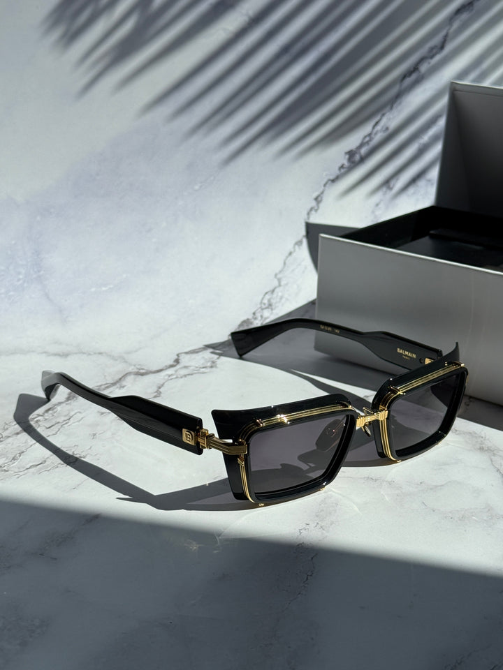 Balmain black square sunglasses with dark lenses and gold trim, laid out