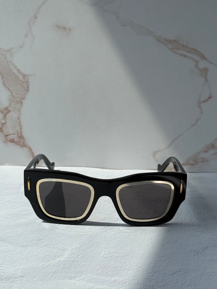 Front view of black square sunglasses with dark lenses and gold-tone trim.