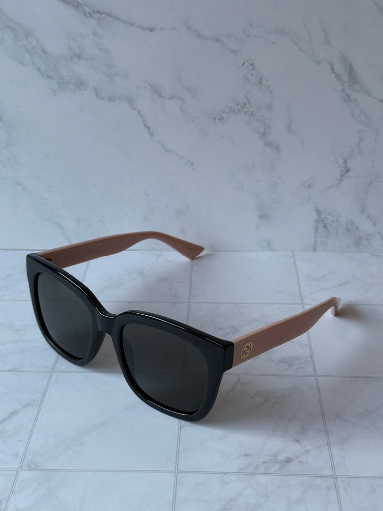 Cat-eye sunglasses with black frames, pink arms, dark lenses, Gucci logo