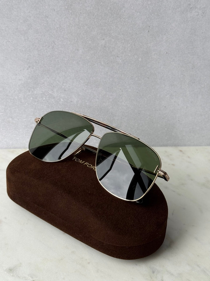 Rose gold sunglasses with green lenses, resting on brown protective case