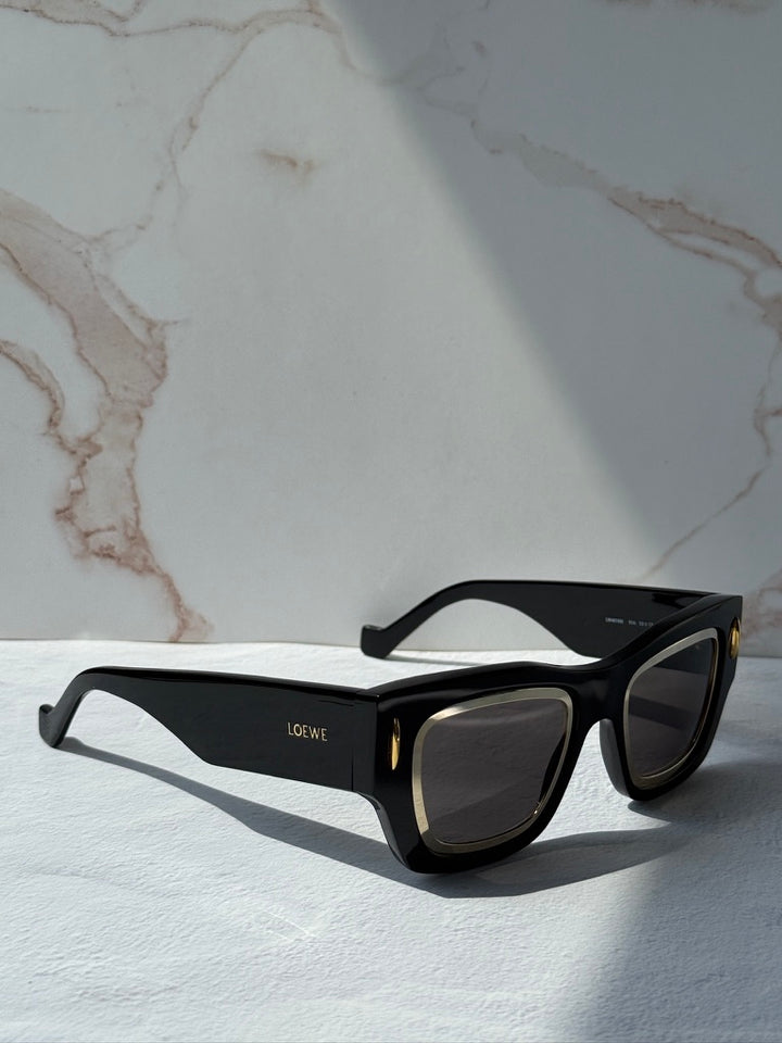 Black square sunglasses with dark lenses and gold-tone trim, shown from the opposite angle.