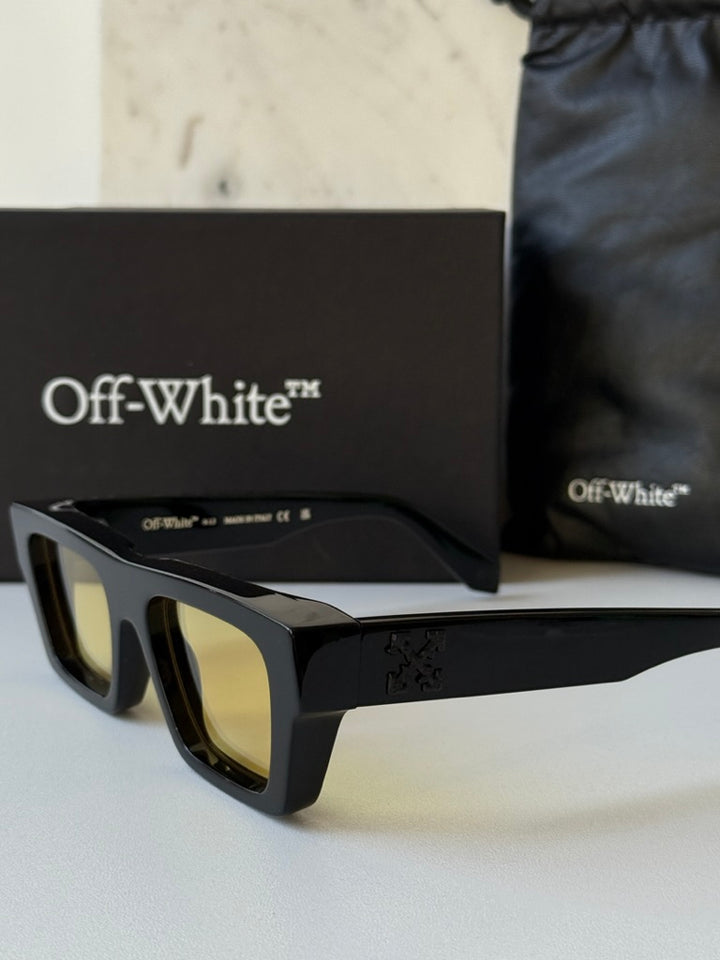 Black sunglasses with yellow lenses on a display with branded box and pouch