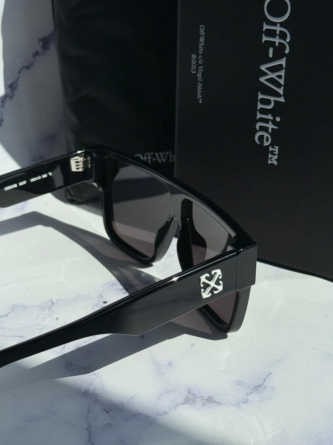 Black square sunglasses angled view with dark lenses and temple logo