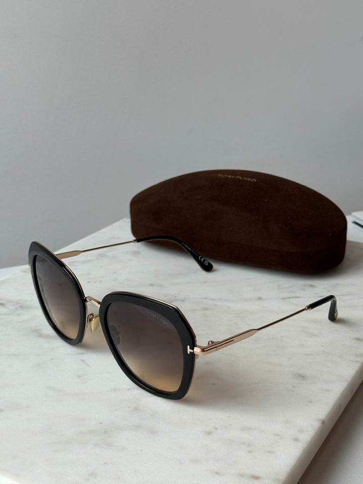 Tom Ford black and gold sunglasses with dark lenses, side angle beside case