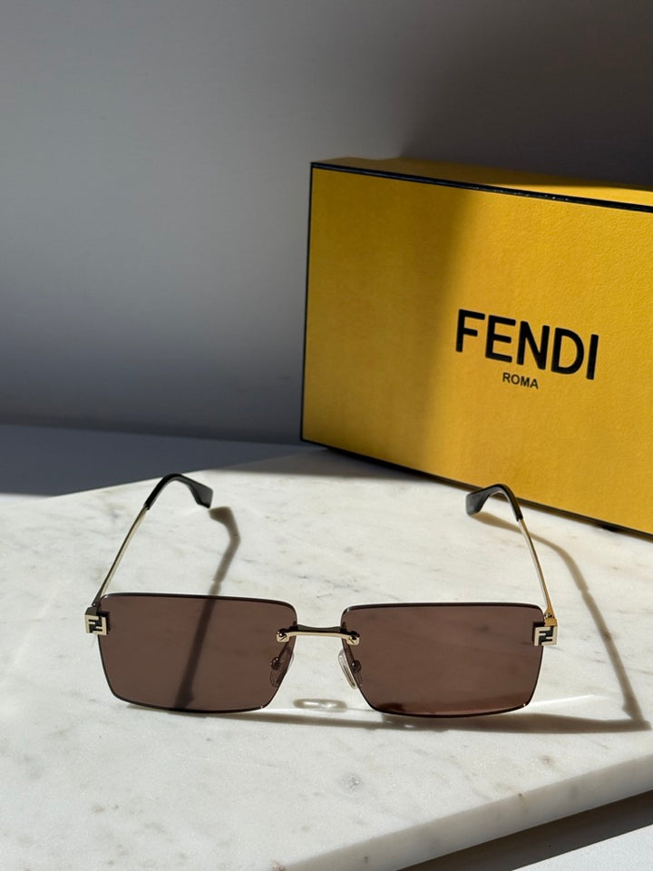 Rimless rectangular sunglasses with brown lenses and gold metal frame, black temples