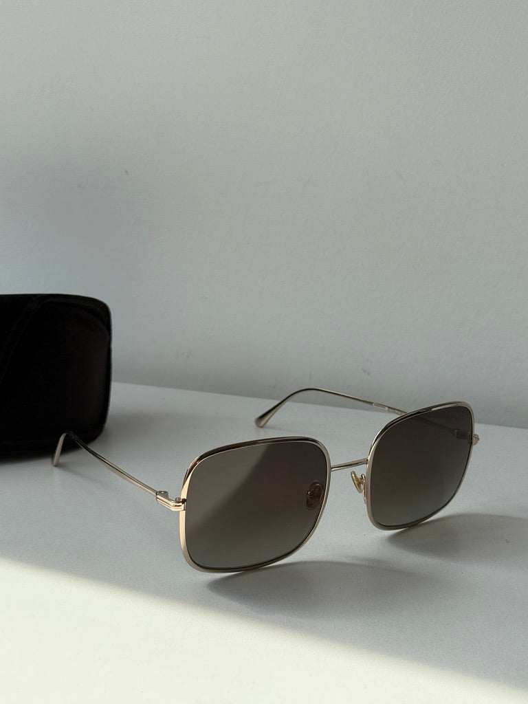 Gold square sunglasses with dark lenses on white surface.
