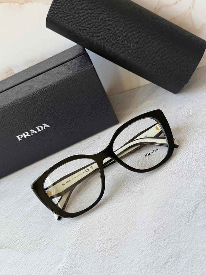 Black cat-eye eyeglasses frames with clear lenses and gold-toned logo details.