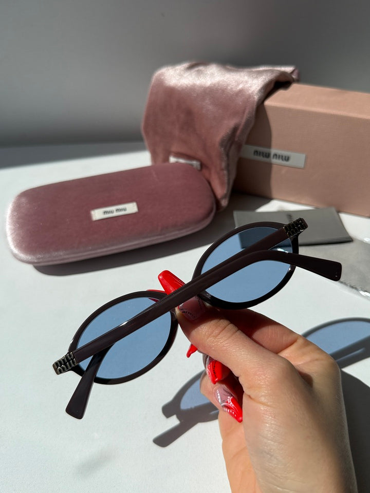 Oval sunglasses with blue lenses and dark frames, hand adjusting temple