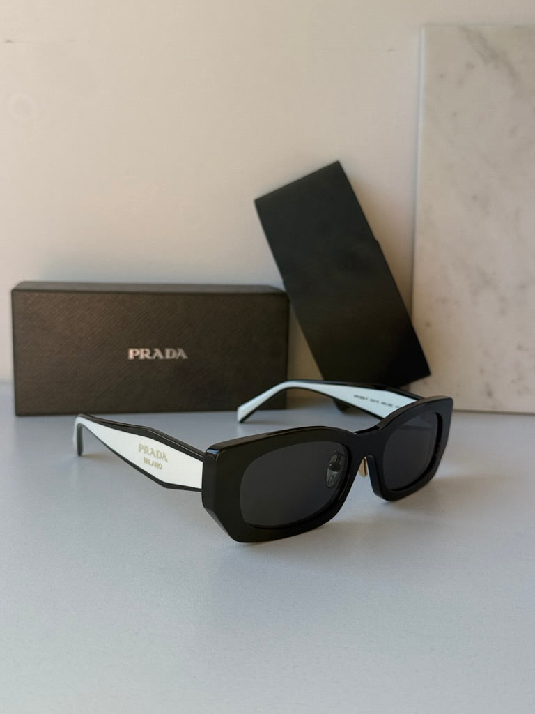 Prada black sunglasses with dark lenses, white temple arms and case packaging.