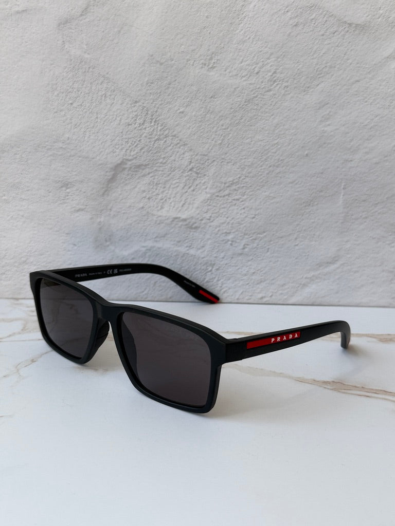 Black polarized rectangular sunglasses, side view; dark lenses and red logo bar on temple