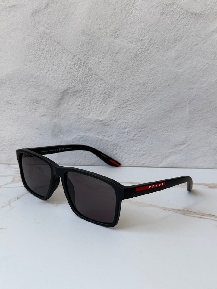 Black polarized rectangular sunglasses, side view; dark lenses and red logo bar on temple
