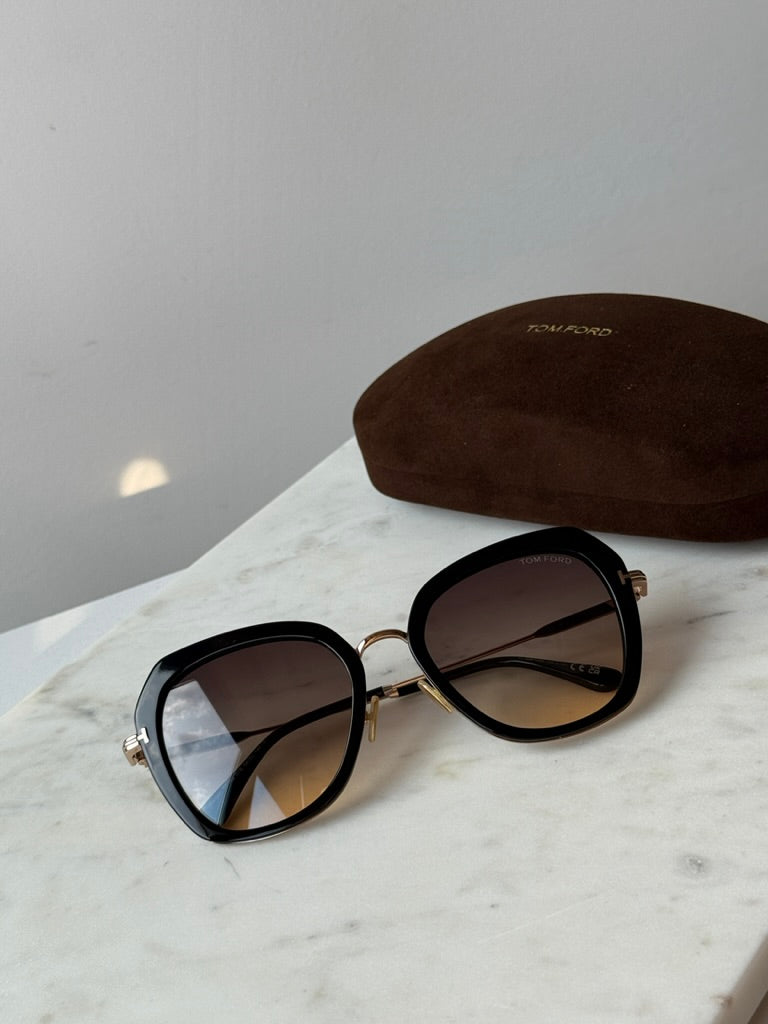 Tom Ford black and gold sunglasses with brown case, top view over dark tinted lenses