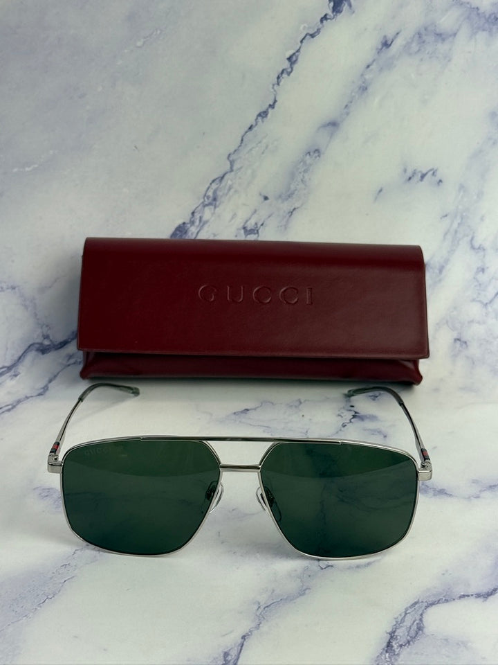 Silver metal aviator sunglasses with green lenses, red Gucci case behind