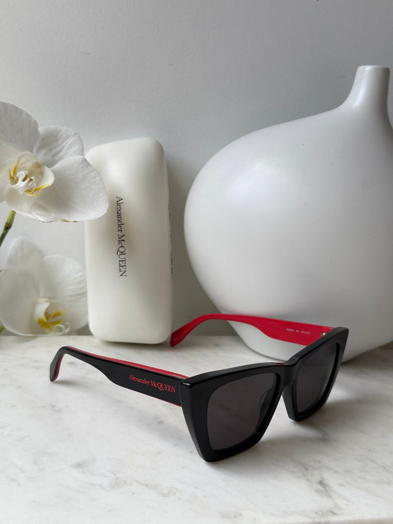 Black cat-eye sunglasses with dark lenses and red temple arms, angled view