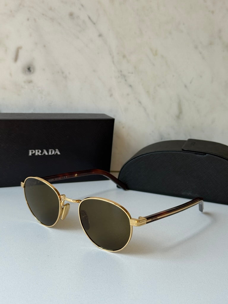 Prada round sunglasses with gold frame and dark brown mirrored lenses, resting on display
