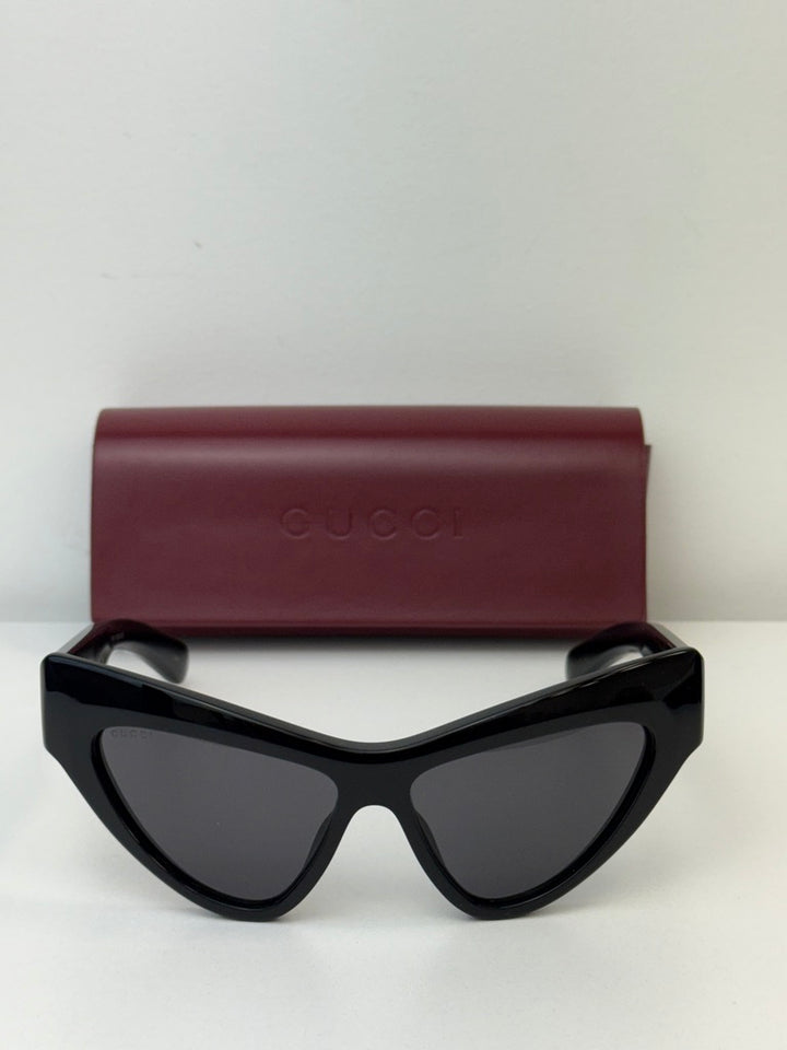 Gucci black cat-eye sunglasses with dark lenses beside burgundy case