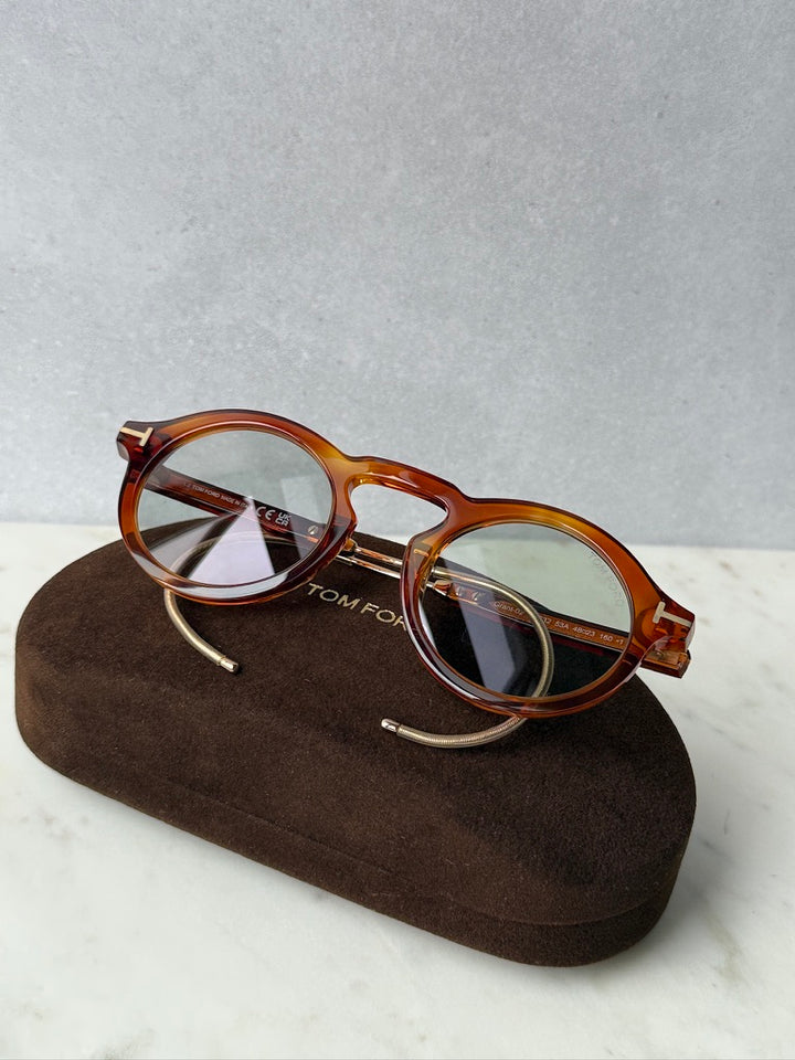 Brown tortoise round sunglasses resting on a brown case with gold-tone temples