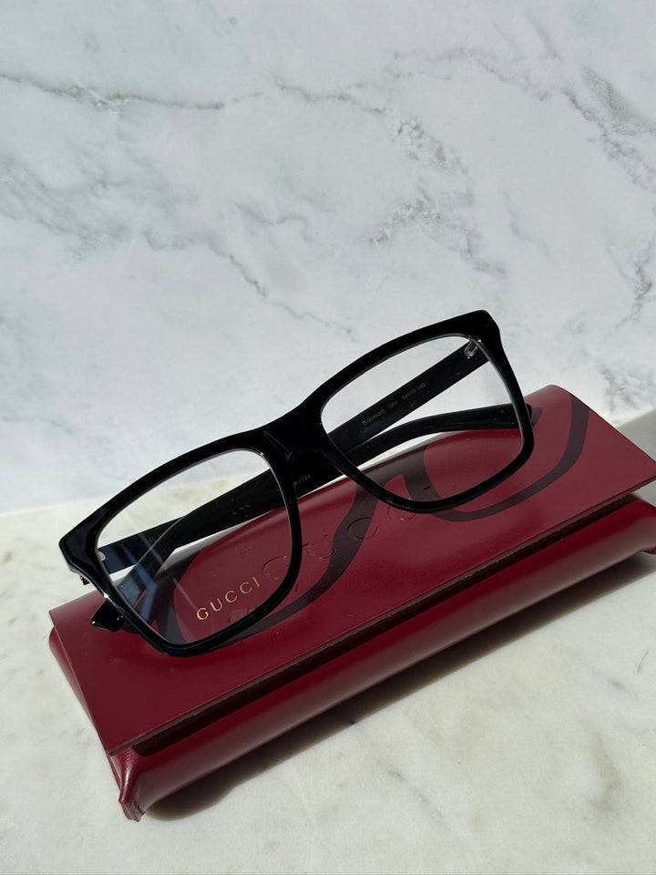 Black rectangular eyeglass frames with clear lenses and Gucci branding on temples