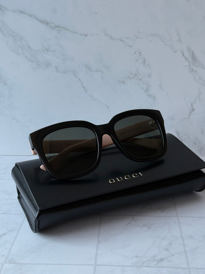 Sunglasses with black frames, pink accents, and dark lenses, Gucci branding on case