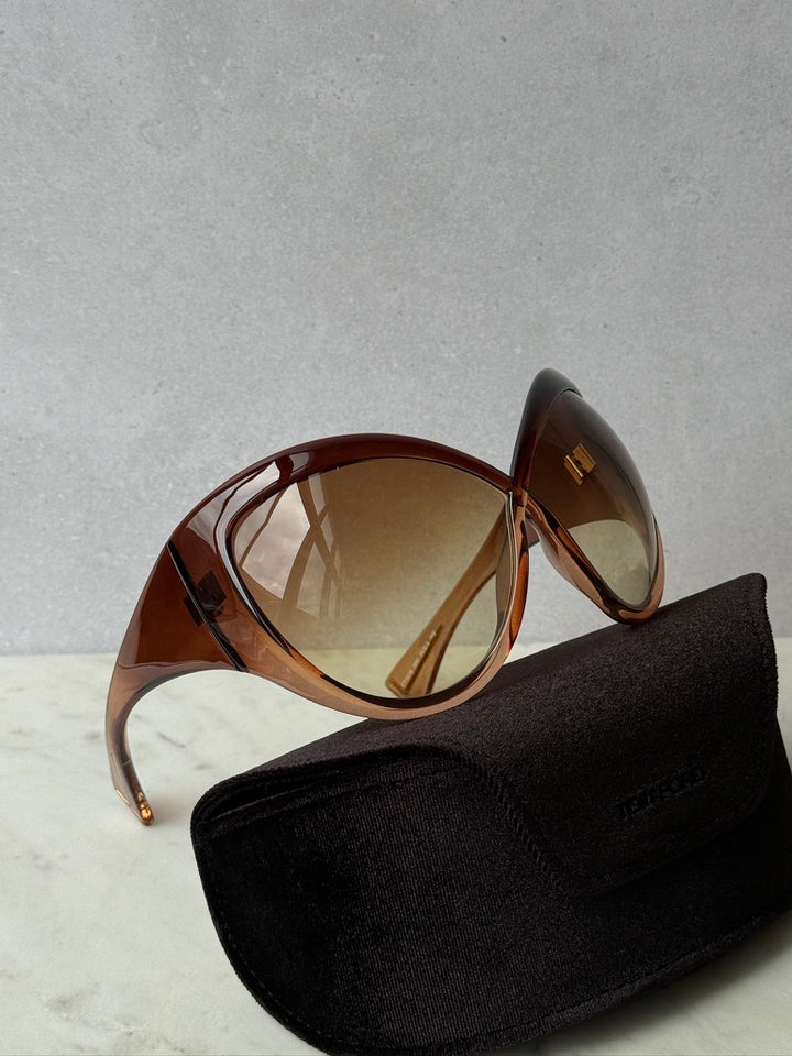 Brown oversized mask sunglasses with gradient lenses beside a black case