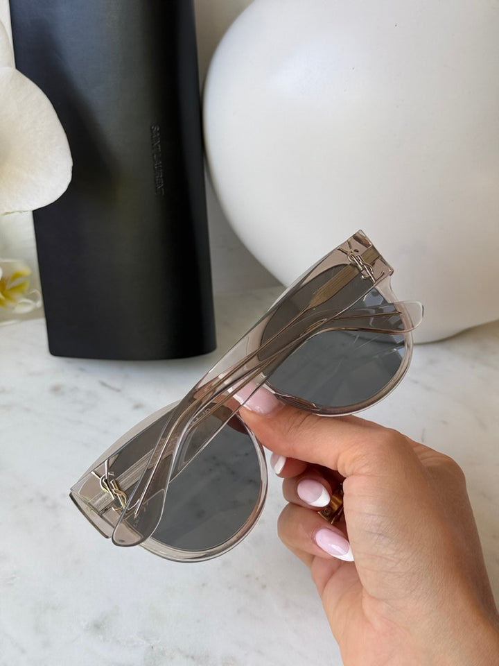 Cat-eye sunglasses in clear silver with dark tinted lenses, hand holding