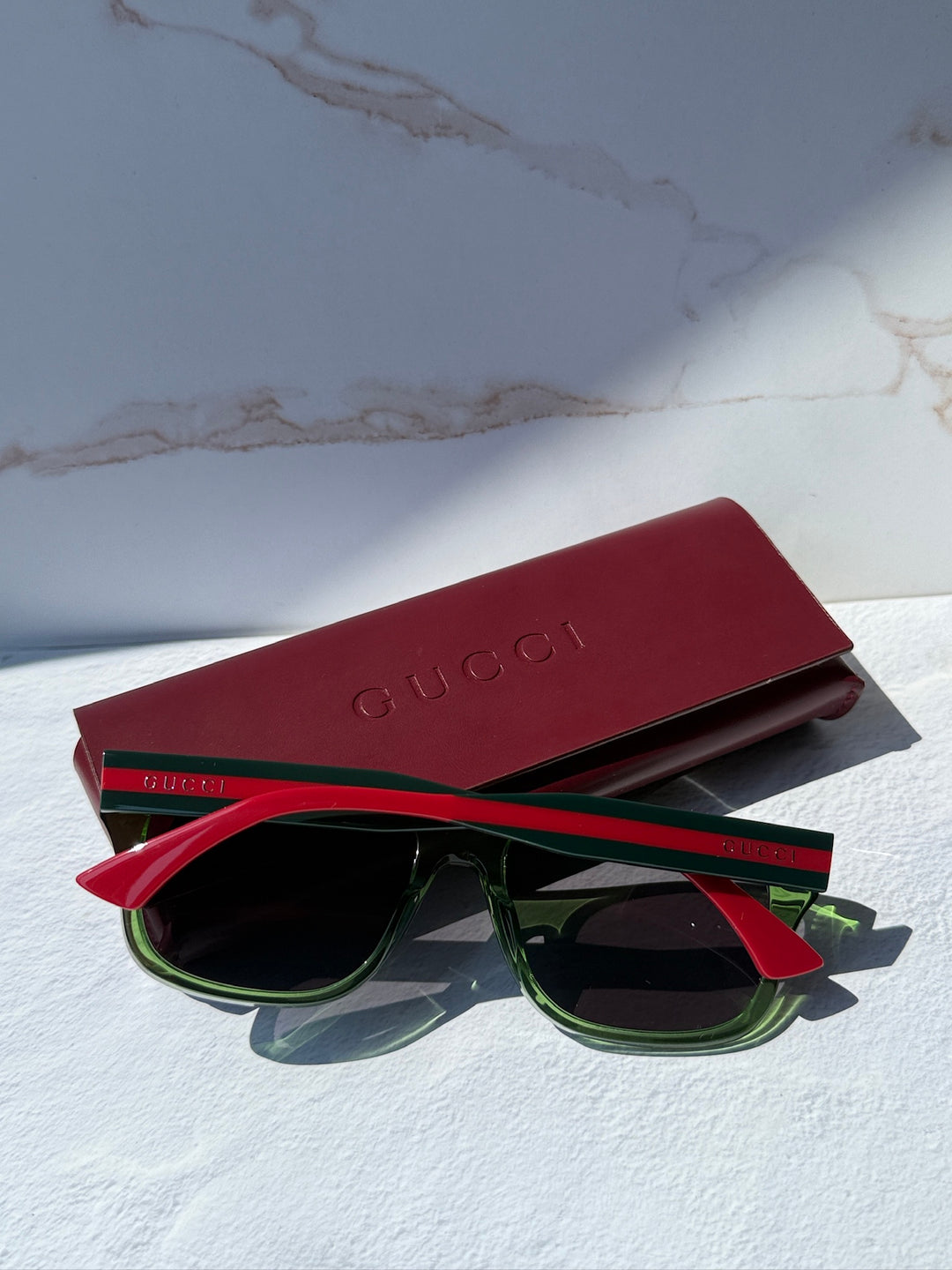 Gucci striped sunglasses with green frame and dark lenses, red temples, burgundy case.
