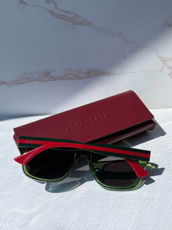 Gucci striped sunglasses with green frame and dark lenses, red temples, burgundy case.