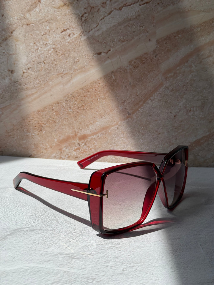 Burgundy square sunglasses laid down, tinted gradient lenses and gold-tone accents