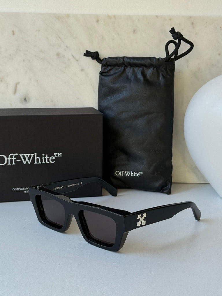 Black sunglasses with dark lenses and Off-White temple logo, near pouch and box