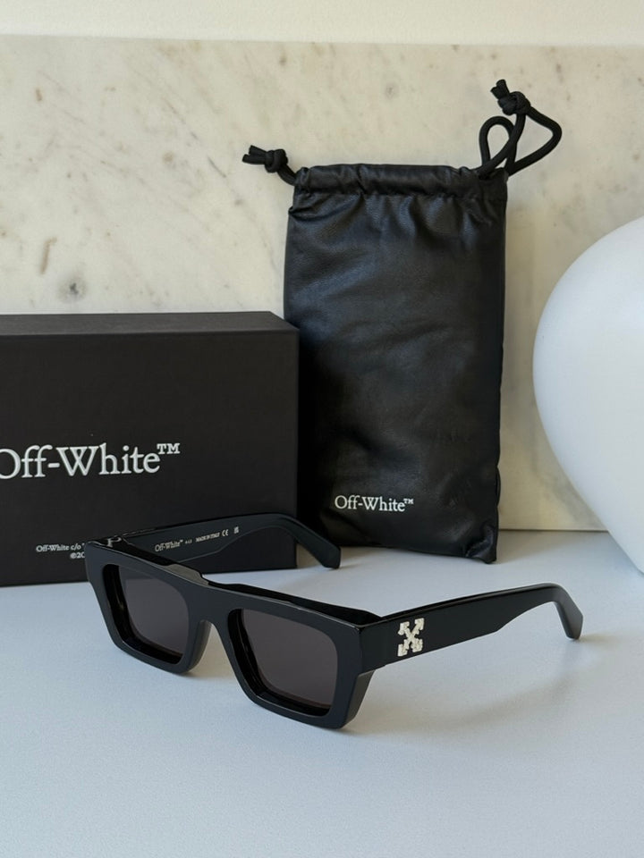 Black sunglasses with dark lenses and Off-White temple logo, near pouch and box