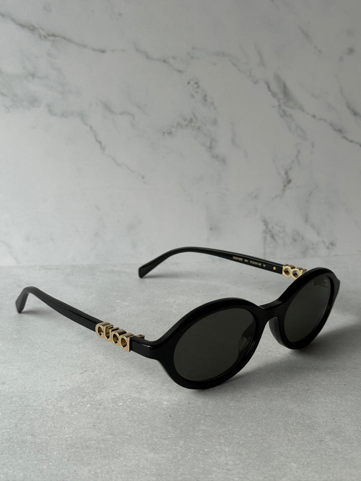Black oval sunglasses with dark lenses and GUCCI gold logo details on temples