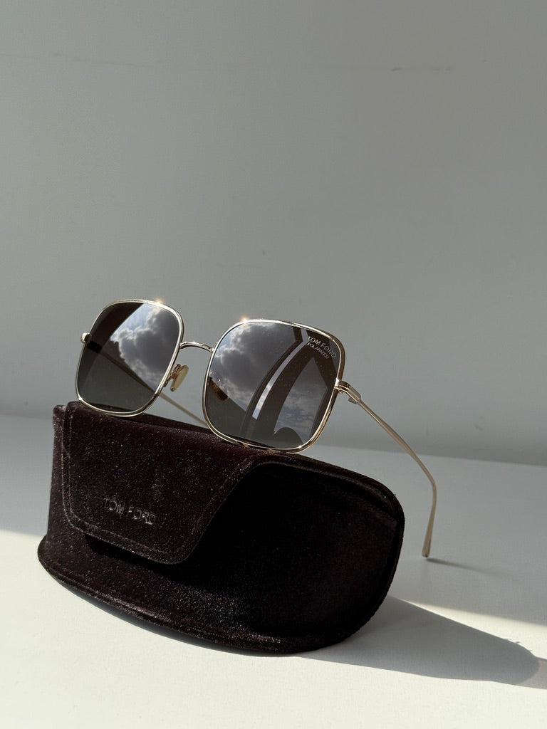 Gold sunglasses with dark lenses resting in velvet case.
