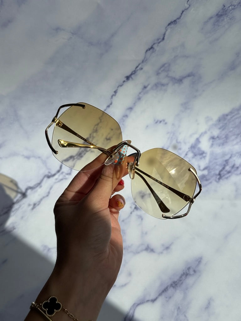 Gucci rimless sunglasses close-up, gold frame with yellow lenses in hand