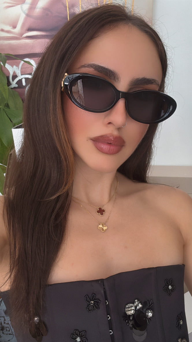 Black oval sunglasses with dark lenses and gold logo hinge, front three-quarter