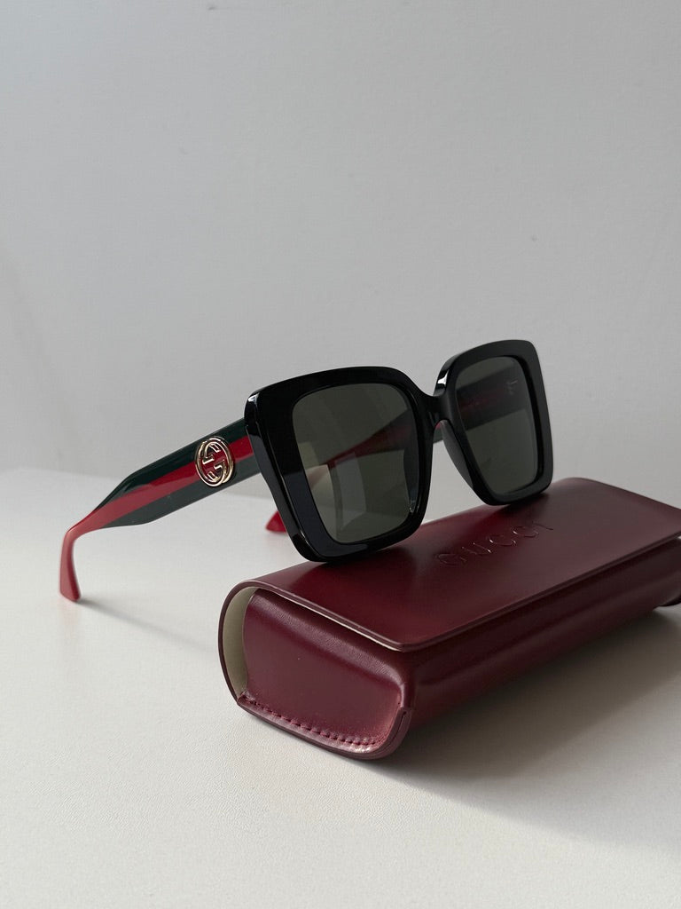 Oversized black sunglasses with dark lenses and red temple accents, on case