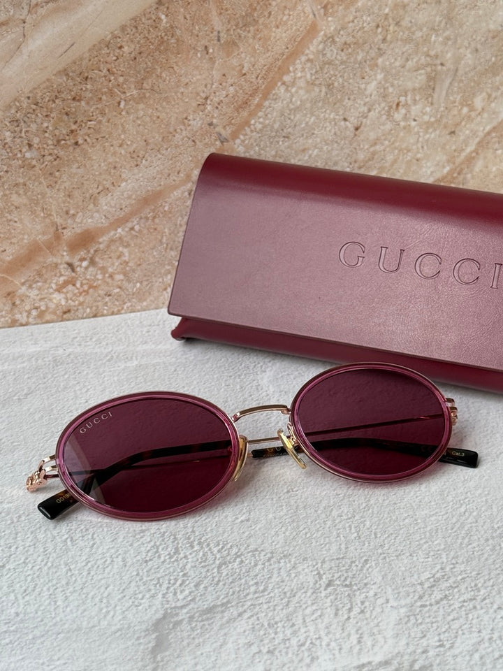 Gucci oval pink sunglasses with dark lenses beside pink Gucci case