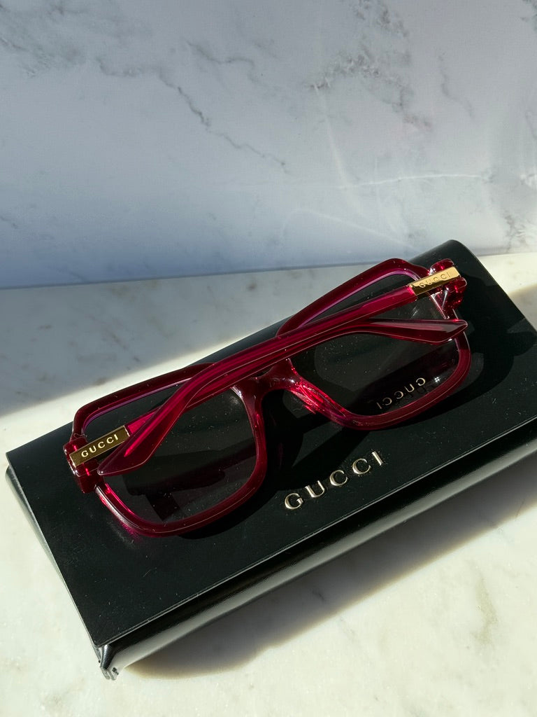 Pink red oversized square eyeglasses laid on a black Gucci box, front view