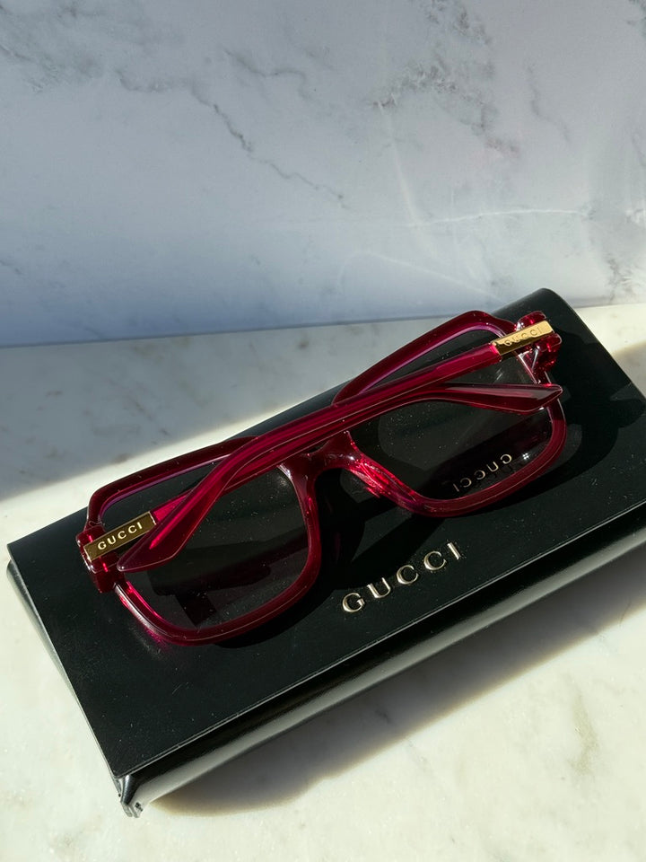 Pink red oversized square eyeglasses laid on a black Gucci box, front view