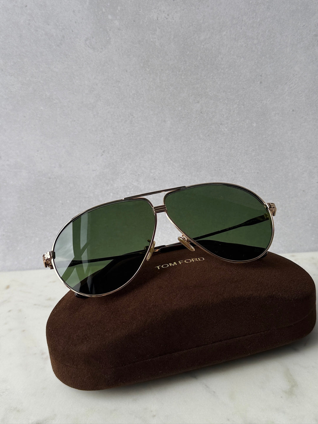 Rose gold aviator sunglasses with green lenses resting on a brown case