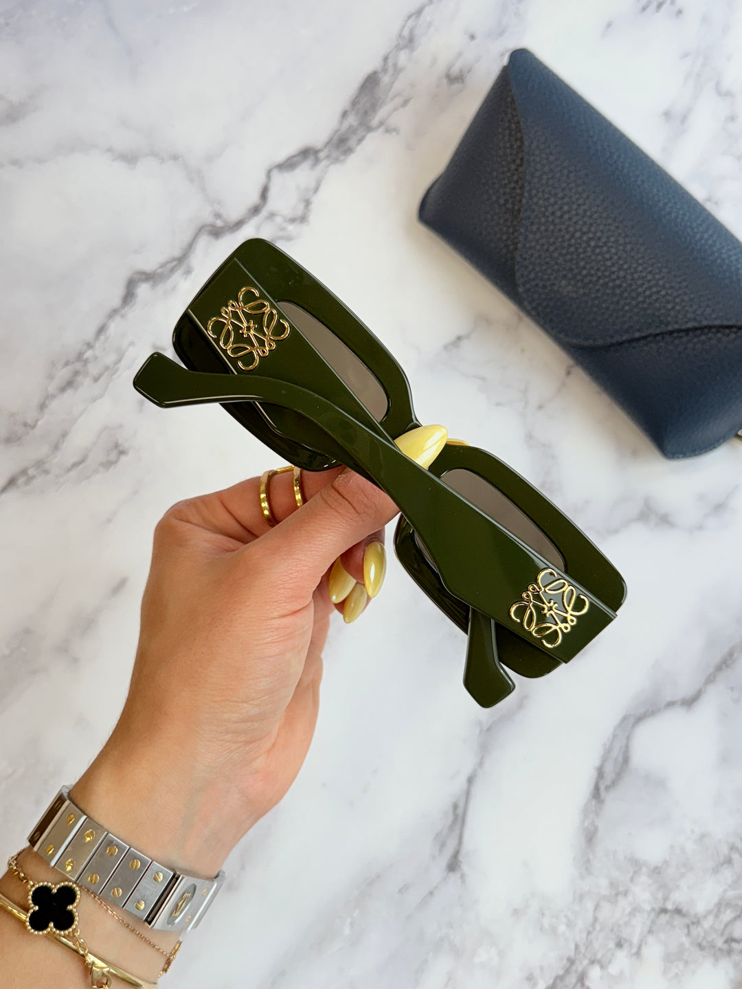 Dark green square sunglasses with gold anagram logo, side view with blue case